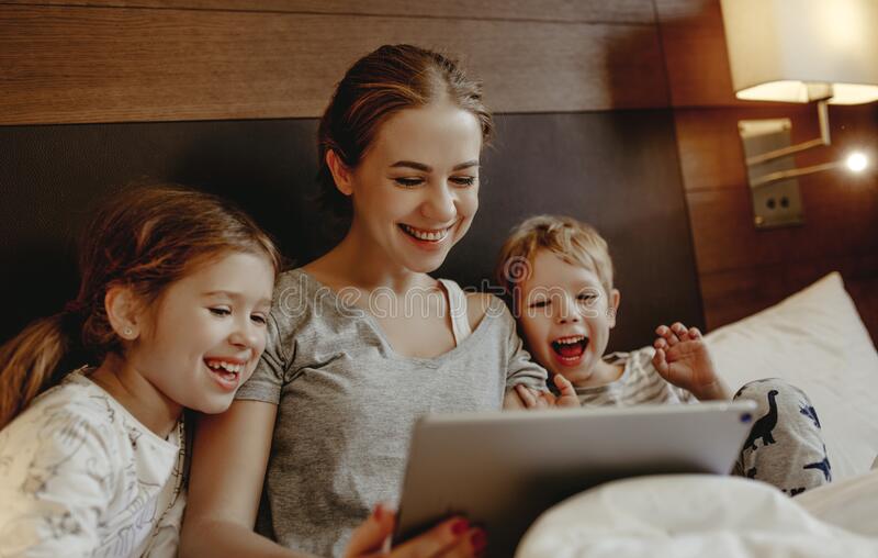 feliz-família-mãe-e-crianças-com-tablet-computer-em-casa-na-cama-à-noite-169065861